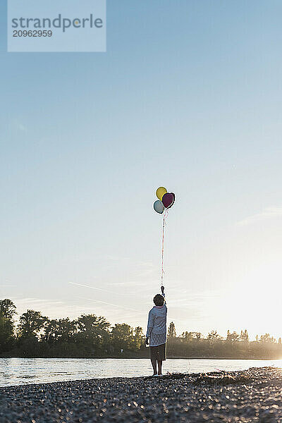 Senior woman holding balloons at riverbank