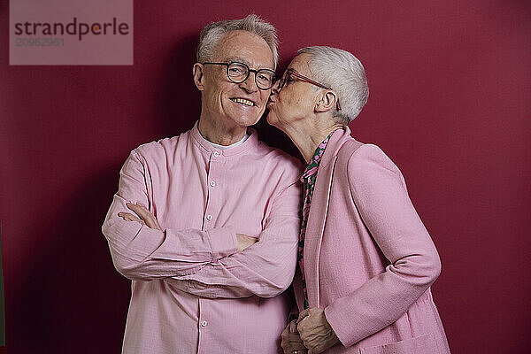 Senior woman kissing man against purple background