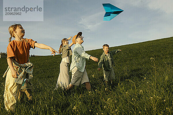 Happy siblings playing with paper plane in meadow