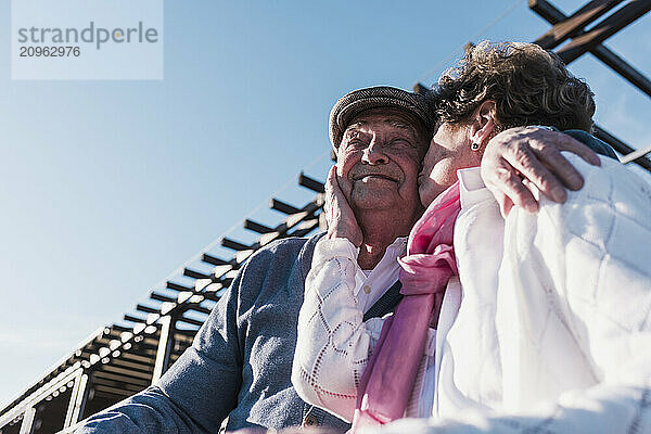 Senior woman kissing man under sky on sunny day