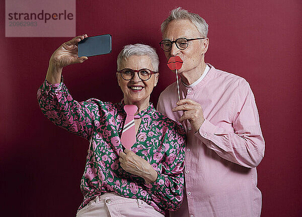 Happy senior couple with fake lips and tie taking selfie