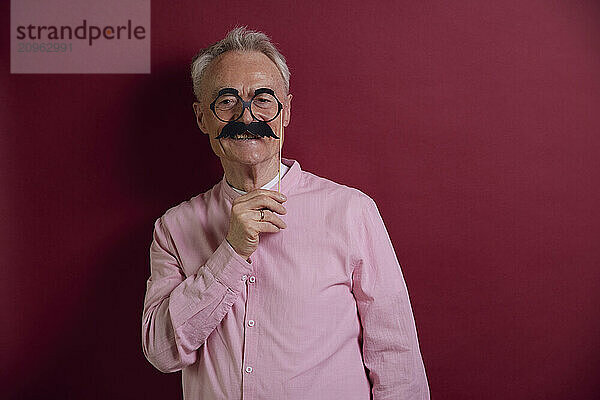 Senior man posing with fake moustache against purple background