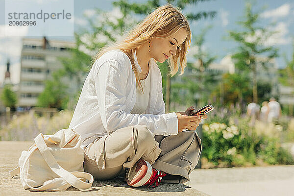 Young woman sitting and using smart phone on street