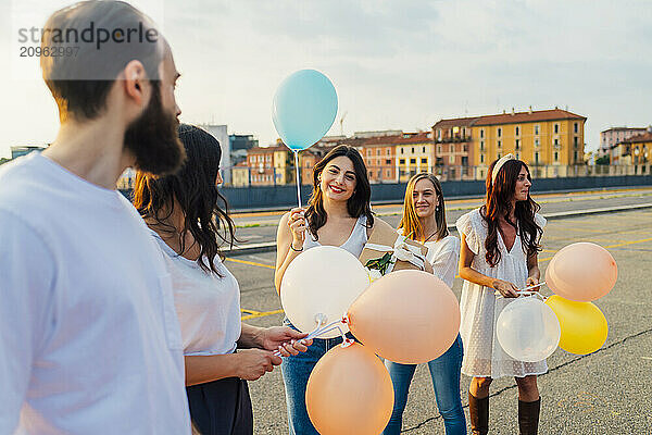 Happy friends standing with balloons on road