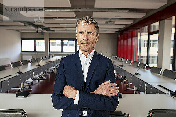 Confident businessman standing with arms crossed in meeting room