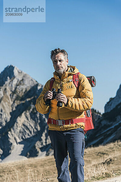 Mature man holding binocular and standing on mountain