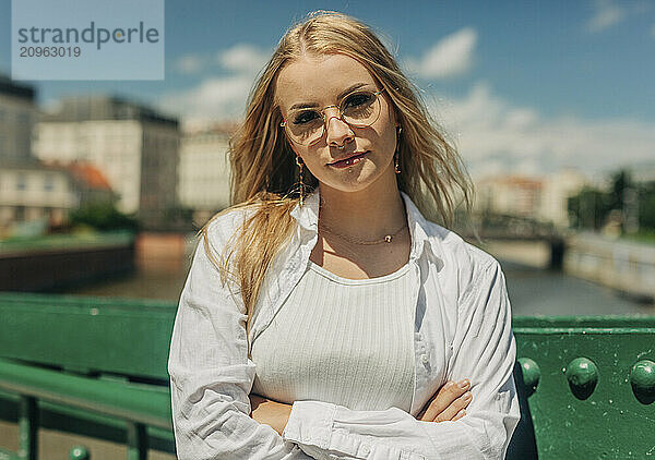 Fashionable young woman with arms crossed near bridge