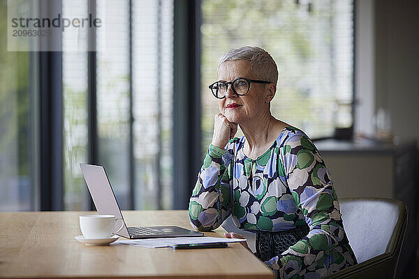 Senior woman sitting at table at home with laptop