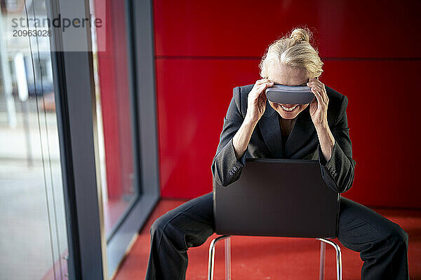 Blond senior businesswoman wearing virtual reality headset sitting on chair