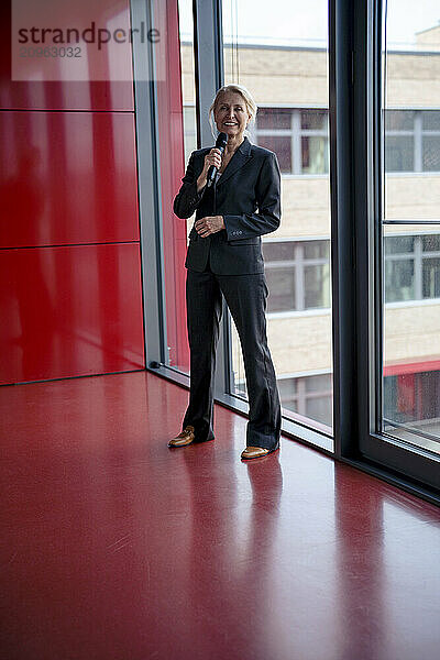 Smiling businesswoman speaking on microphone standing at office