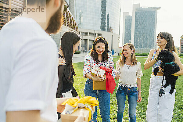 Happy friends giving gifts to woman in park