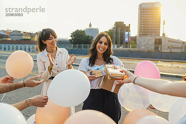 Happy woman taking gifts from friends and celebrating birthday at sunset