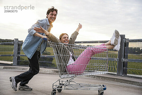 Smiling young man pushing girlfriend sitting in shopping trolley