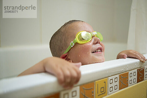 Boy wearing swimming goggles playing in bathtub at home