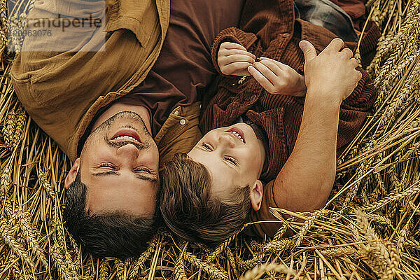 Father and son lying on wheat field from top view  smiling and bonding during harvest.