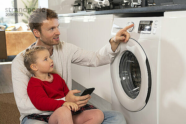 Father teaching daughter to operate washing machine through smart phone app at home