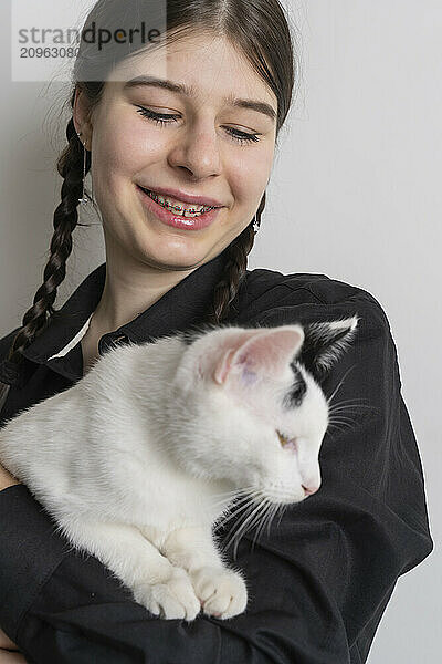 Teenage girl with braces smiling and holding a white cat indoors.