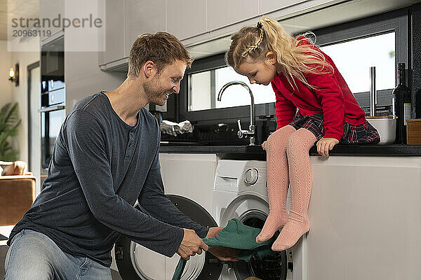 Father doing laundry with daughter in kitchen at home