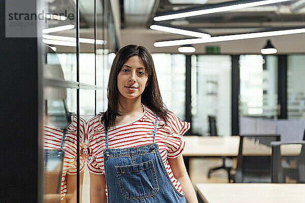 Confident businesswoman leaning on wall at office