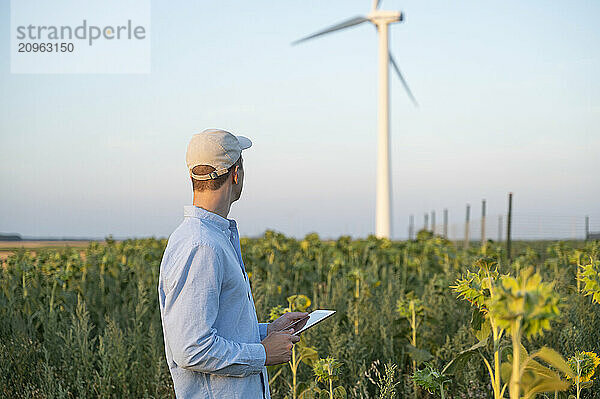 Young engineer holding tablet PC and standing in field