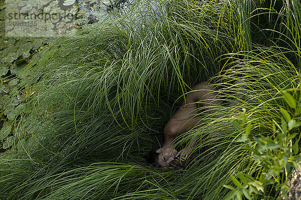 Naked woman lying down in swamp near pond