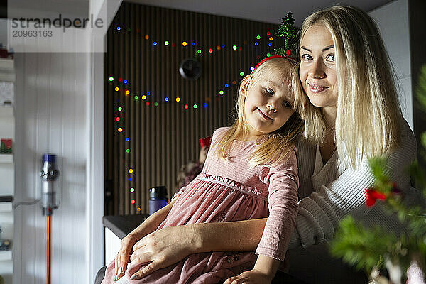 Daughter sitting on lap of mother at home