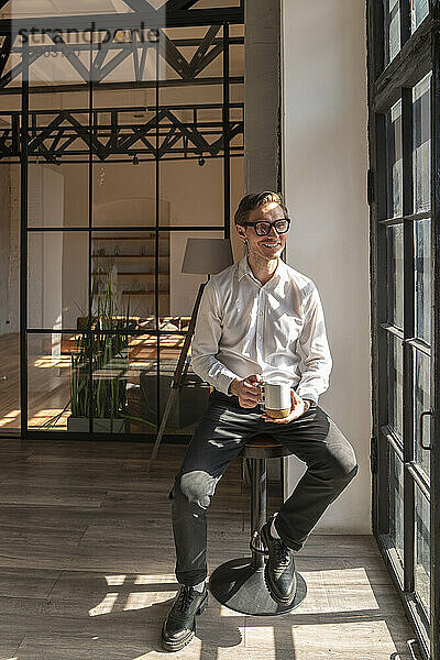 Happy businessman sitting with coffee cup in office