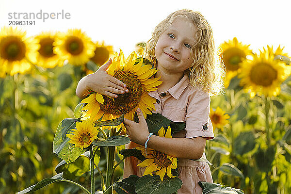 Smiling blond hair girl holding sunflower in field