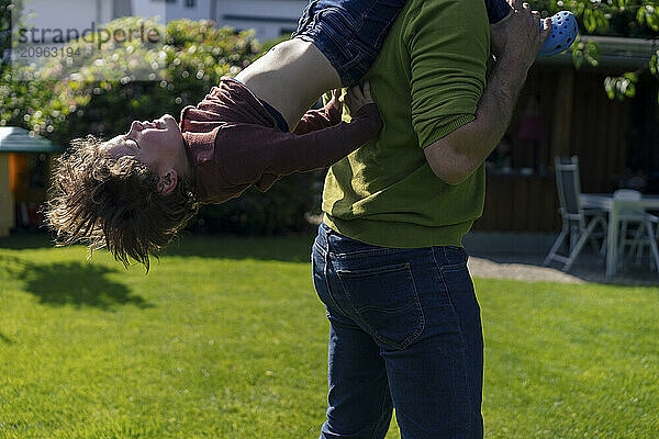 Father carrying son on shoulders and spending leisure time in back yard