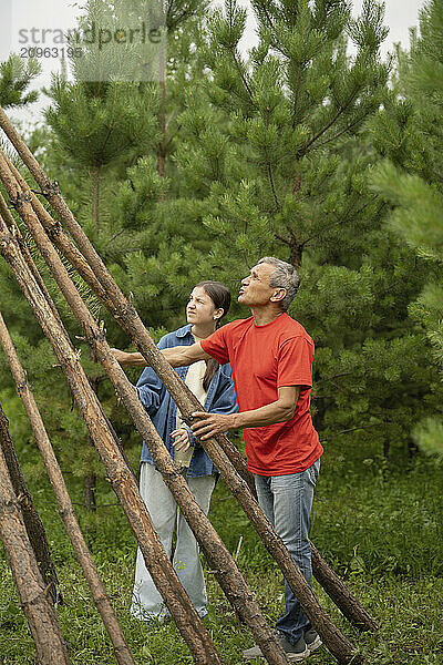 Grandfather and grand daughter making hut in forest