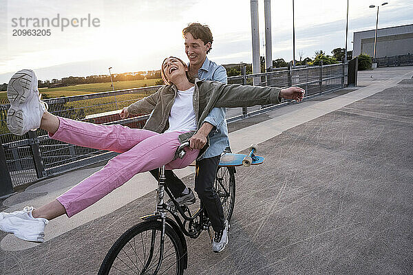 Carefree woman sitting on handlebar with boyfriend riding bicycle at parking lot