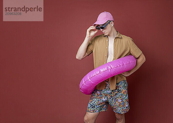 Young man wearing sunglasses posing with swimming float against brown background