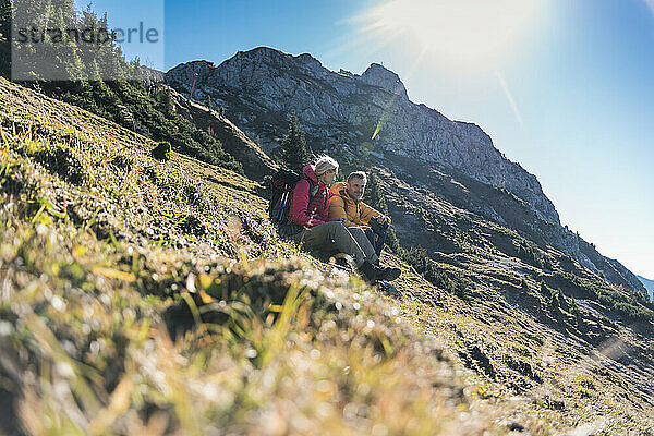 Friends sitting on mountain at sunny day