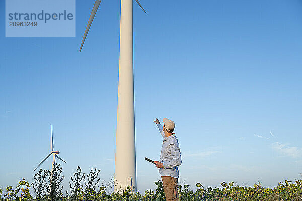 Maintenance engineer standing and pointing at wind turbine in field