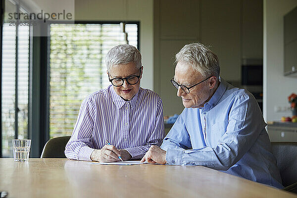 Senior couple sitting at table at home examining document