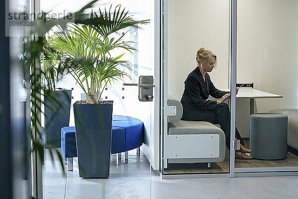 Senior businesswoman using tablet PC sitting in office cubicle