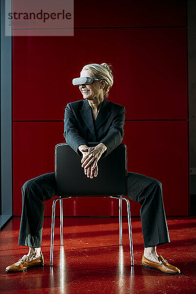 Smiling businesswoman wearing virtual reality headset sitting on chair