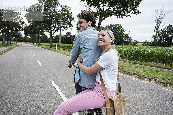 Cheerful young woman embracing boyfriend sitting on bicycle