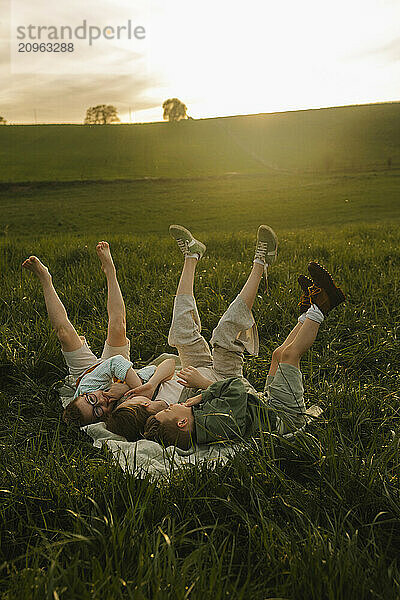 Siblings with legs up lying on grass at meadow