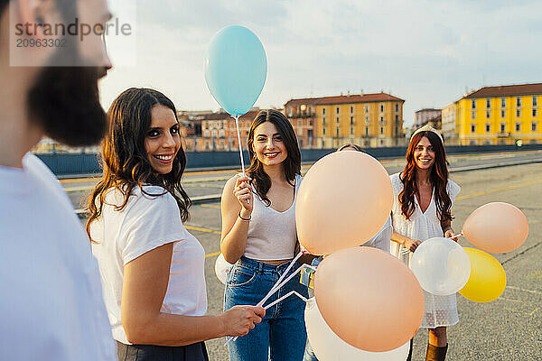 Happy friends standing with balloons and having fun on road