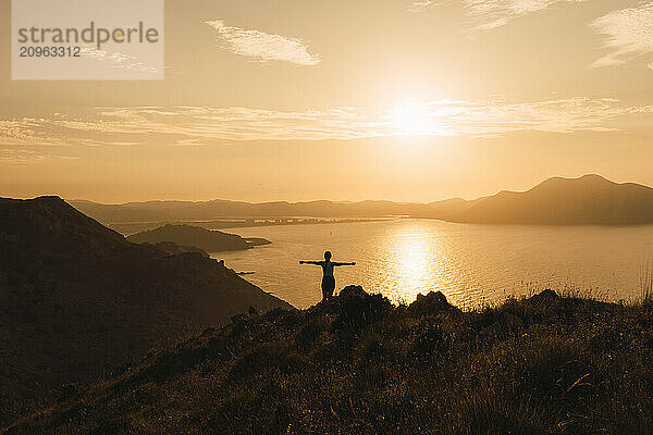 Young woman standing with arms outstretched at sunrise near river