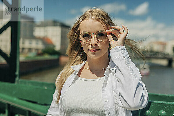 Blond woman holding eyeglasses near bridge