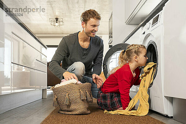 Father looking at daughter loading clothes in washing machine at home