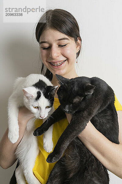 Teenage girl with braces holding two cats and enjoying time together at home.