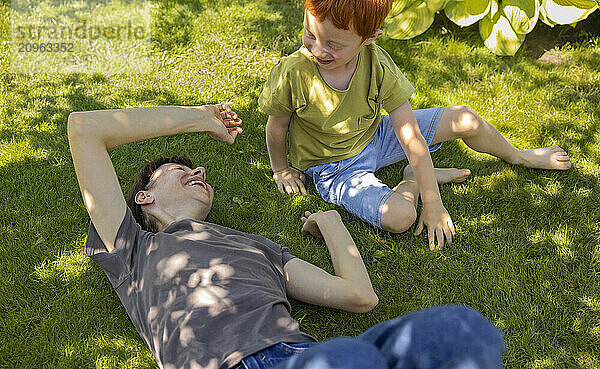 Mother lying on grass and playing with son in garden