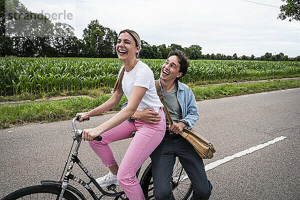 Cheerful young man embracing girlfriend sitting on bicycle