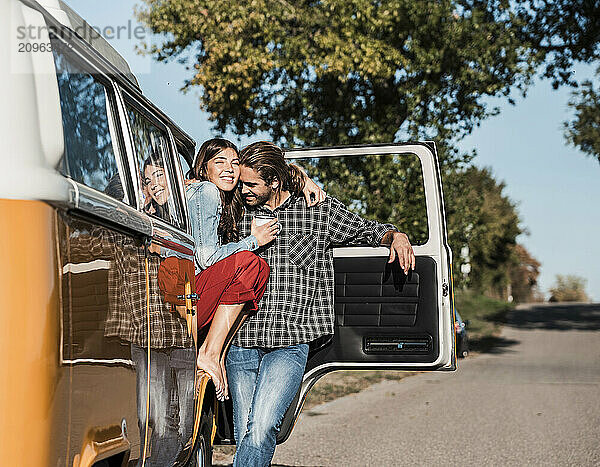 Young man with arm around girlfriend standing outside van on road