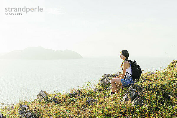 Young backpacker looking at view and sitting on mountain