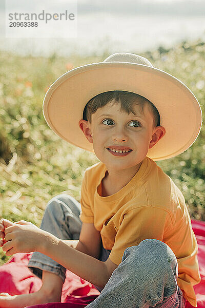 Young boy in hat sitting in meadow on sunny day