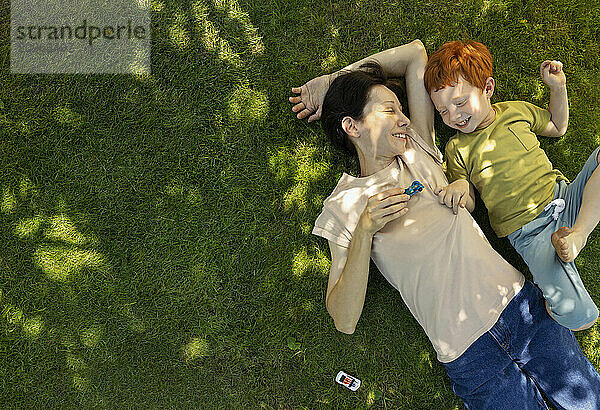 Happy mother and son lying on grass and playing with toys in garden